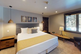 Manor Vail 163 bedroom with a king size bed and a wood framed window with snow-capped mountains in the distance.