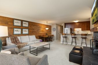 A spacious open concept living area featuring a sofa, armchairs, coffee table, dining area, kitchen bar, and a fireplace.