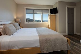 A cozy bedroom at Ranch at Steamboat RA220 with a made bed, a large window offering an exterior view, a wall-mounted TV, and a wooden cabinet.