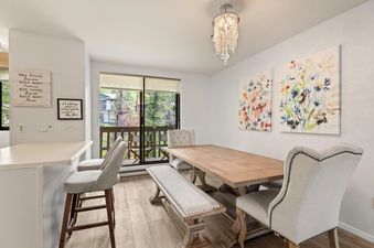 Bright and elegant dining area in Riverview Unit 22 featuring a rustic wooden table, upholstered seating, and a crystal chandelier.