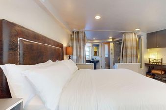 The primary bedroom at Montaneros 411 features a large bed with a leather headboard and an en-suite bathroom with a pedestal sink and shower, along with a dedicated desk area.