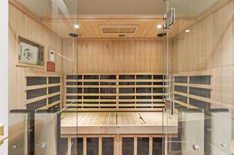 A private indoor sauna with light wood paneling, slatted benches, and a clear glass door, offering a serene and warm retreat.