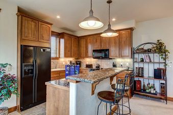 A kitchen with wood cabinets, granite countertops, and a breakfast bar with two stools.