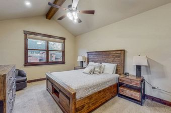A spacious bedroom featuring a rustic wooden bed with a light-colored comforter, several pillows, and two wooden nightstands with lamps.