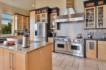 The kitchen at Sky Villa features stainless steel appliances, granite countertops, and light wood cabinetry, with a large window offering an exterior view.