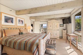 A cozy bedroom in Enclave 207 with a log-style bed, striped bedding, rustic furniture, and large windows offering a view of the outdoors.