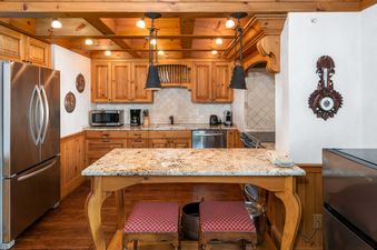 The kitchen in Chateau Christian 2 Bedroom Platinum Unit 310 features wooden cabinetry, stainless steel appliances, a granite island, and exposed wooden beams.