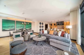 A wide shot of One Snowmass Residence Club 407's open-concept living room, dining area, and kitchen, featuring modern furnishings and vibrant art.