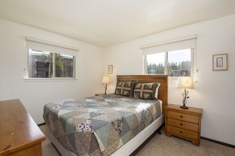 The bedroom at Hi Country Haus 2115 features a queen-sized bed with a quilted bedspread and two windows.