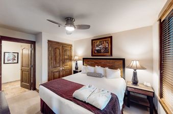 A cozy bedroom with a king-size bed, warm lamp lighting, and wooden furniture in BlueSky Breckenridge 402.