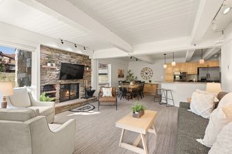 The inviting open-concept living and dining area of Enclave 209, featuring a stone fireplace, comfortable seating, and a modern kitchen.