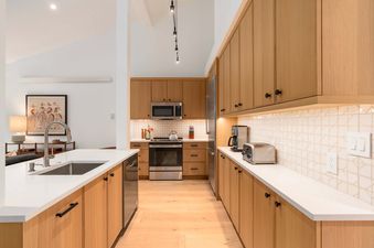 A modern kitchen with warm wood cabinetry, white countertops, and stainless steel appliances at Cottonwood Jackson Hole.