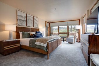 An inviting bedroom in Chateau Chamonix CX111 featuring a plush bed with a leather headboard, elegant artwork, and large windows with scenic views.