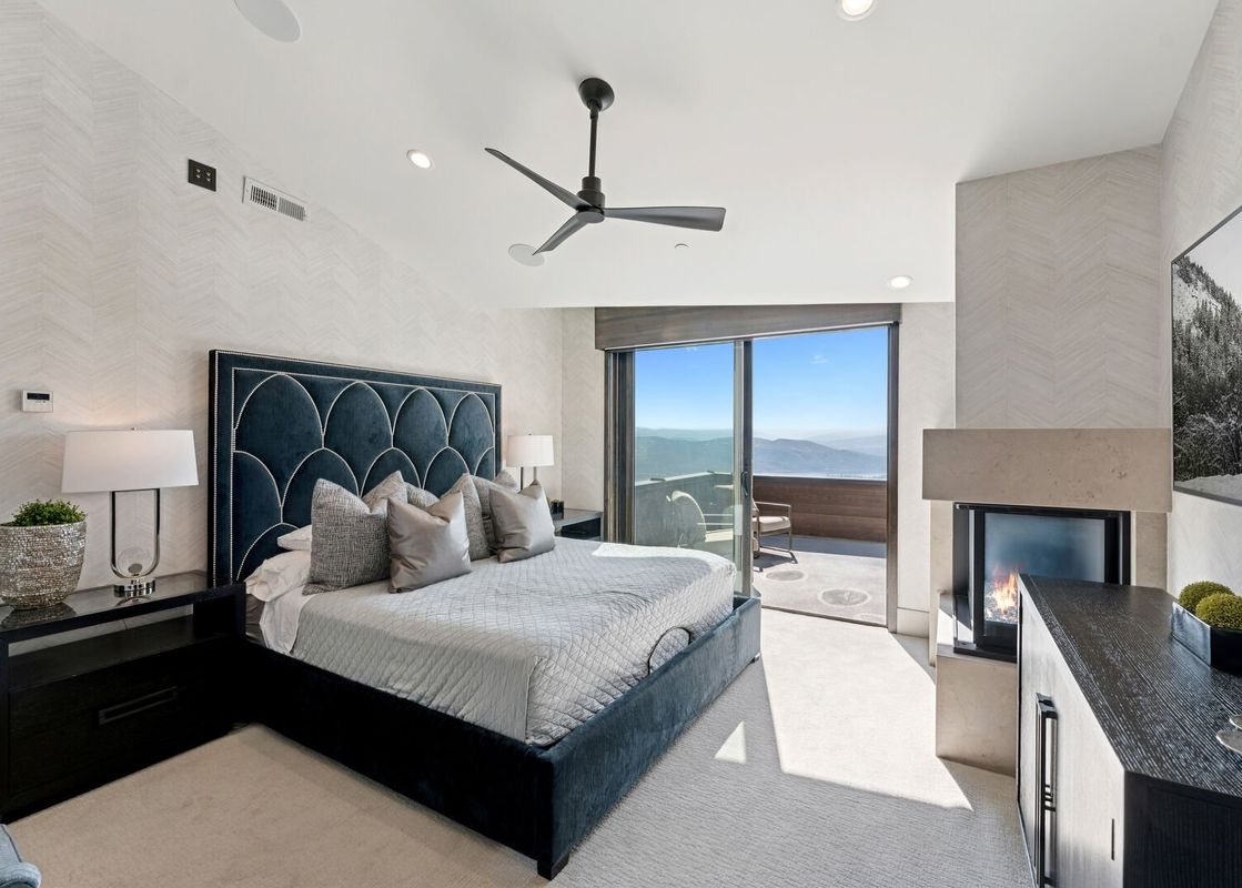A luxurious bedroom featuring a king-sized bed, a fireplace, and a private balcony with stunning mountain views.