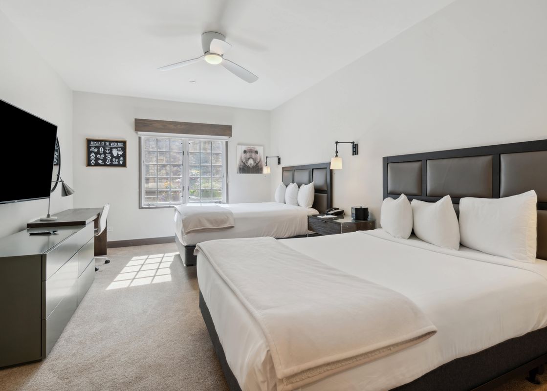 A hotel bedroom at The Charter F235 with two queen beds, a desk, and a television.