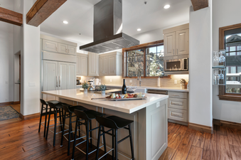 The kitchen of Grand Lodge Four Bedroom 302 has a large island with bar stools, a stainless steel range hood, and a view of the snowy mountains outside the window.