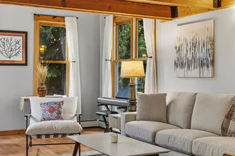 Cozy living room in Town Charm featuring a gray sectional sofa, white armchair, and exposed wooden ceiling beams.