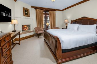 A luxurious bedroom in Arrabelle 460 featuring a king-sized sleigh bed, a cozy fireplace, a television, and elegant wooden furnishings.