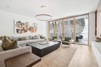 An elegant living area in Founders Place 2403, featuring an L-shaped sofa, two armchairs, a large coffee table, and an expansive view of a snow-covered landscape through sliding glass doors.