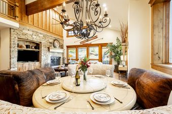A large, rustic living and dining area featuring a stone fireplace, a television, and a dining table set for guests.