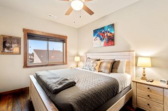 A king-sized bed with a quilted bedspread and decorative wolf-themed pillows is shown in a bedroom with a window offering a view of rooftops, alongside vibrant wolf artwork on the walls.