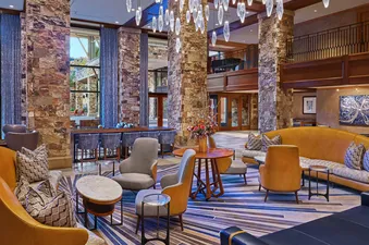 A modern lobby of a hotel with a stone wall, an array of seating, and a large window with a view of trees.