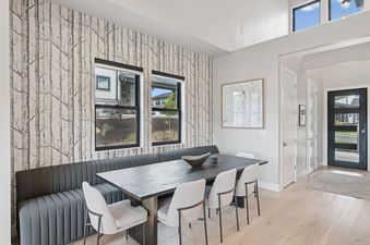 A modern dining area at Deer Valley Vista featuring a dark wooden table with gray seating, birch tree wallpaper, and a view through the windows.