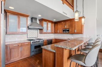 A modern, spacious kitchen in Hummingbird Overlook at Hummingbird Lodge featuring wooden cabinets, granite countertops, a breakfast bar, and stainless steel appliances.