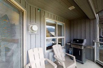 The outdoor patio is furnished with two white chairs, a BBQ grill, and a window with a view of a snowy mountain.