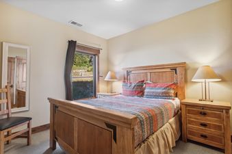 A cozy bedroom in Pines Unit 240 with a wooden bed, colorful bedding, and a window offering an outdoor view.