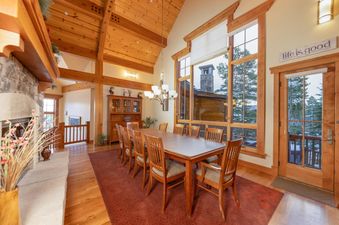 The Timber Trail Lodge dining area features a large wooden table and chairs, a stone fireplace, and large windows with a view of snow-covered trees.