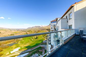 A wide view from a balcony showing a vast landscape with a golf course, mountains, and a clear blue sky.