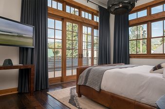 A modern primary bedroom at 5th Street Penthouse with a leather-framed bed and large windows leading to a balcony.
