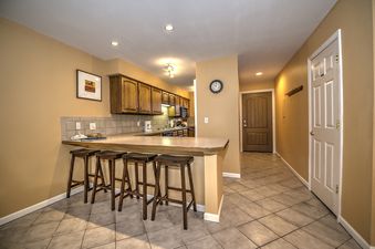 A modern kitchen and dining area with a brown tile floor and an open doorway to a hallway.