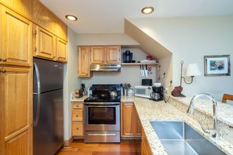 A fully equipped kitchen with light wood cabinets, granite countertops, and stainless steel appliances, including a refrigerator, oven, and microwave.