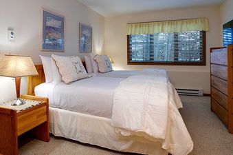 A secondary bedroom at Ranch at Steamboat RA411 with two queen-sized beds, a dresser with a television, and a window with blinds.