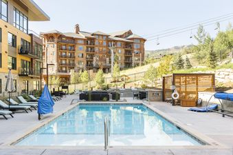 An inviting outdoor pool area at Lift 406, featuring lounge chairs, a BBQ station, and picturesque mountain views.