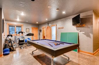 The game room at Alders Chalet features a pool table with cues and billiard balls, exercise equipment, and a table tennis board, offering diverse recreational options.