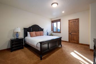 A serene bedroom at Snowtop Manor featuring a dark wood bed with white linens and coral pillows, flanked by dark wood nightstands with blue and white lamps, and a wooden framed window.