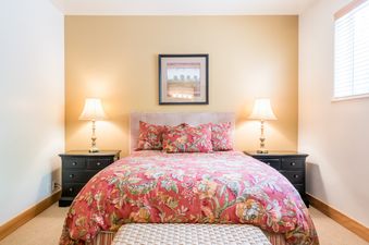 A bedroom with a floral comforter, a small nightstand with lamps on either side, and a picture on the wall