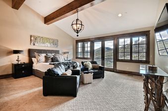 A spacious master bedroom at Powder Haus with a king-sized bed, comfortable seating, mountain views through large windows, and elegant decor.