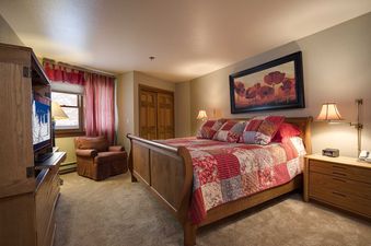 A spacious bedroom at Chateau Chamonix CX124 with a large wooden bed, red and white bedding, a window with red curtains, and a cozy armchair.