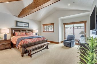 A well-lit and spacious bedroom at The Lookout Home with wood accents, a king-sized bed, and a blue recliner by the window.