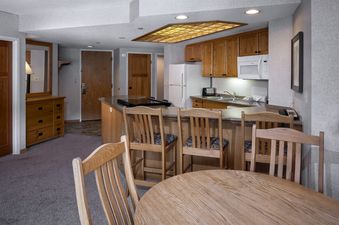 A fully equipped kitchen with wooden cabinets, granite countertops, and a breakfast bar with stools, adjacent to a round dining table in Building 4 Two Bedroom Breckenridge Suite.