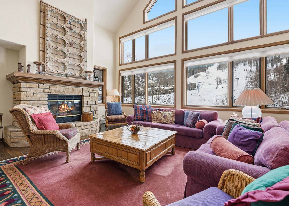 A spacious and elegantly furnished living room at Highlands Slopeside 502, featuring a warm fireplace, plush sofas, and floor-to-ceiling windows with stunning views of snow-covered mountains.