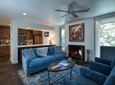 The living area features a comfortable blue sofa, a fireplace, and a coffee table, with a kitchen visible in the background.
