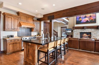 A spacious, open-concept kitchen and living area at Silver Star 47, featuring wooden cabinetry, a large kitchen island with bar stools, a comfortable sectional sofa, and a stone fireplace with a painting above it.