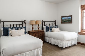Two twin beds are set up in the Moonlight Basin Luxury Suite 6A, featuring white linens and two pillows on each bed. There are two lamps on a wooden dresser between the beds.