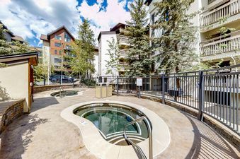 Two outdoor hot tubs at Dulany 105 are surrounded by concrete, with a black metal fence separating them from the residential buildings and evergreen trees.