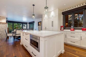 A modern kitchen with white cabinets, a large island with a built-in oven, and a view of the trees outside.